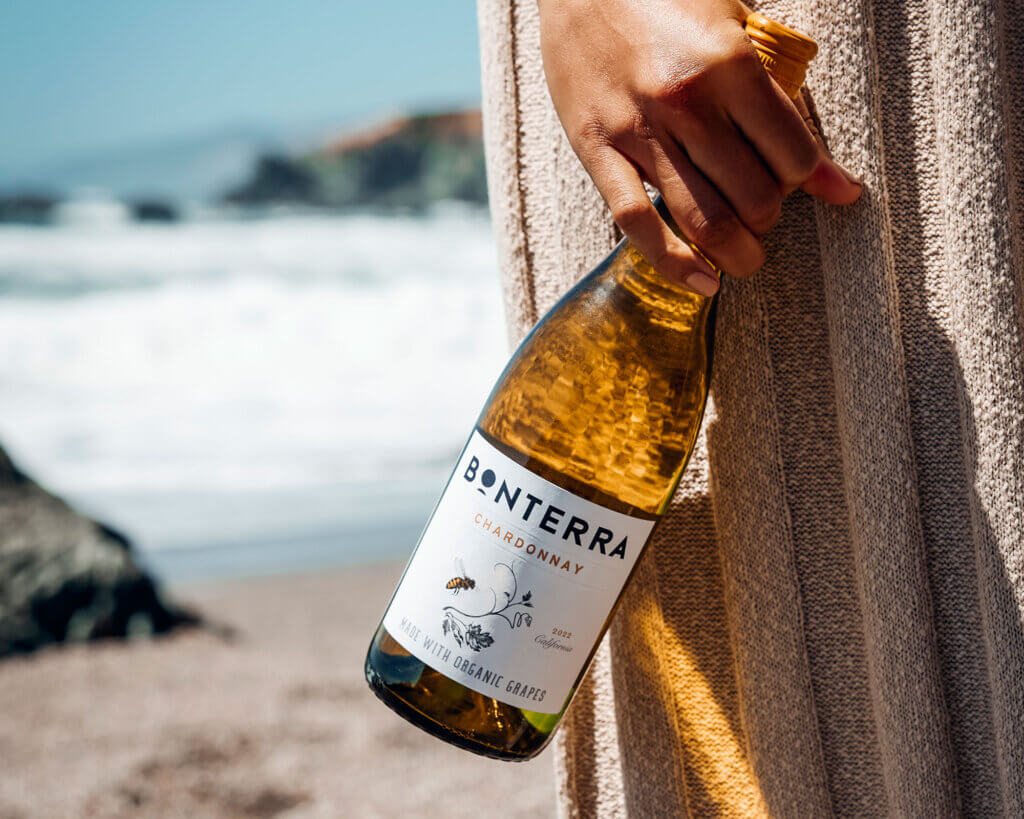 Hand that is holding a bottle of chardonnay on a beach