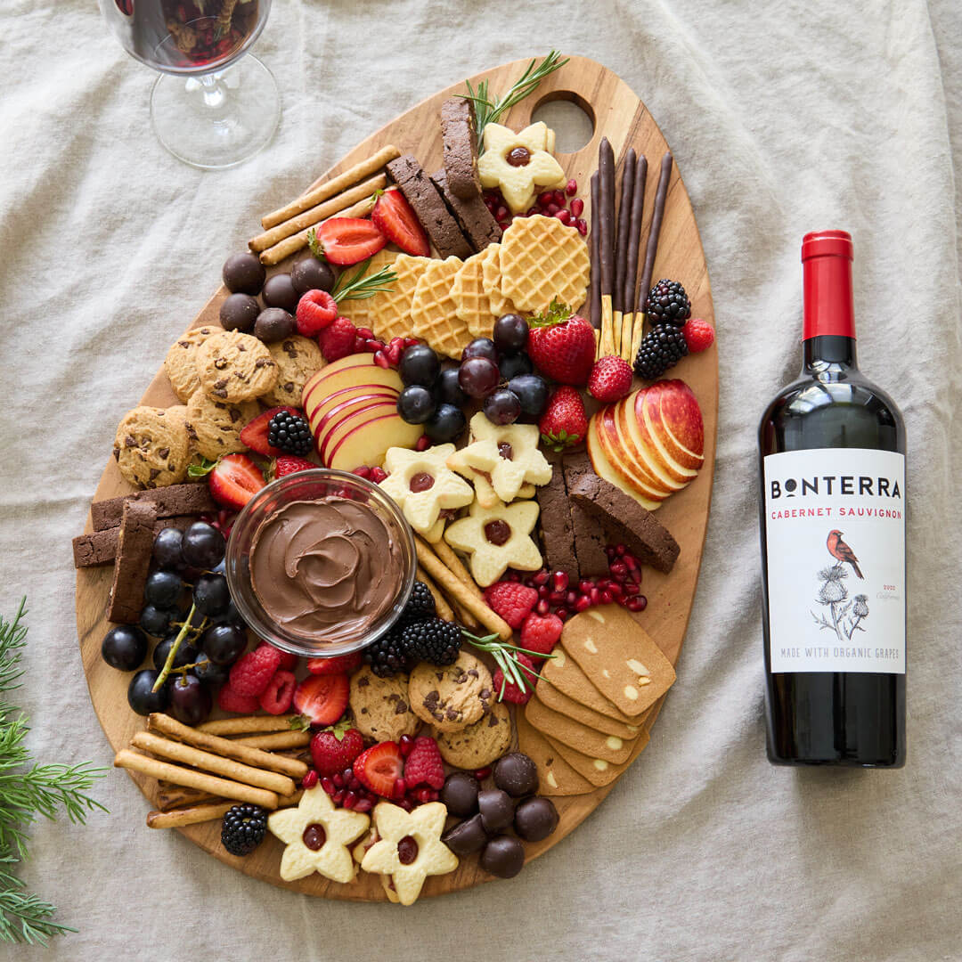 Fresh berries and pomegranate seeds bring a pop of color to this decadent, holiday-inspired grazing board, centered around a creamy chocolate dipping sauce.